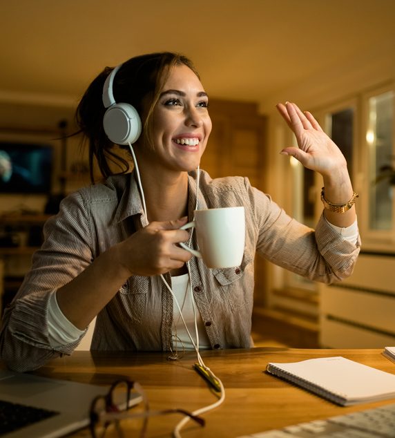 happy-woman-drinking-tea-waving-someone-while-having-video-call-desktop-pc-evening-home